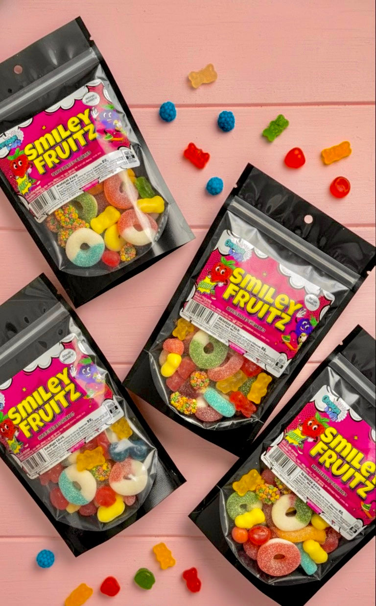 Smiley Fruitz candy packages on a pink background with scattered gummy candies.
